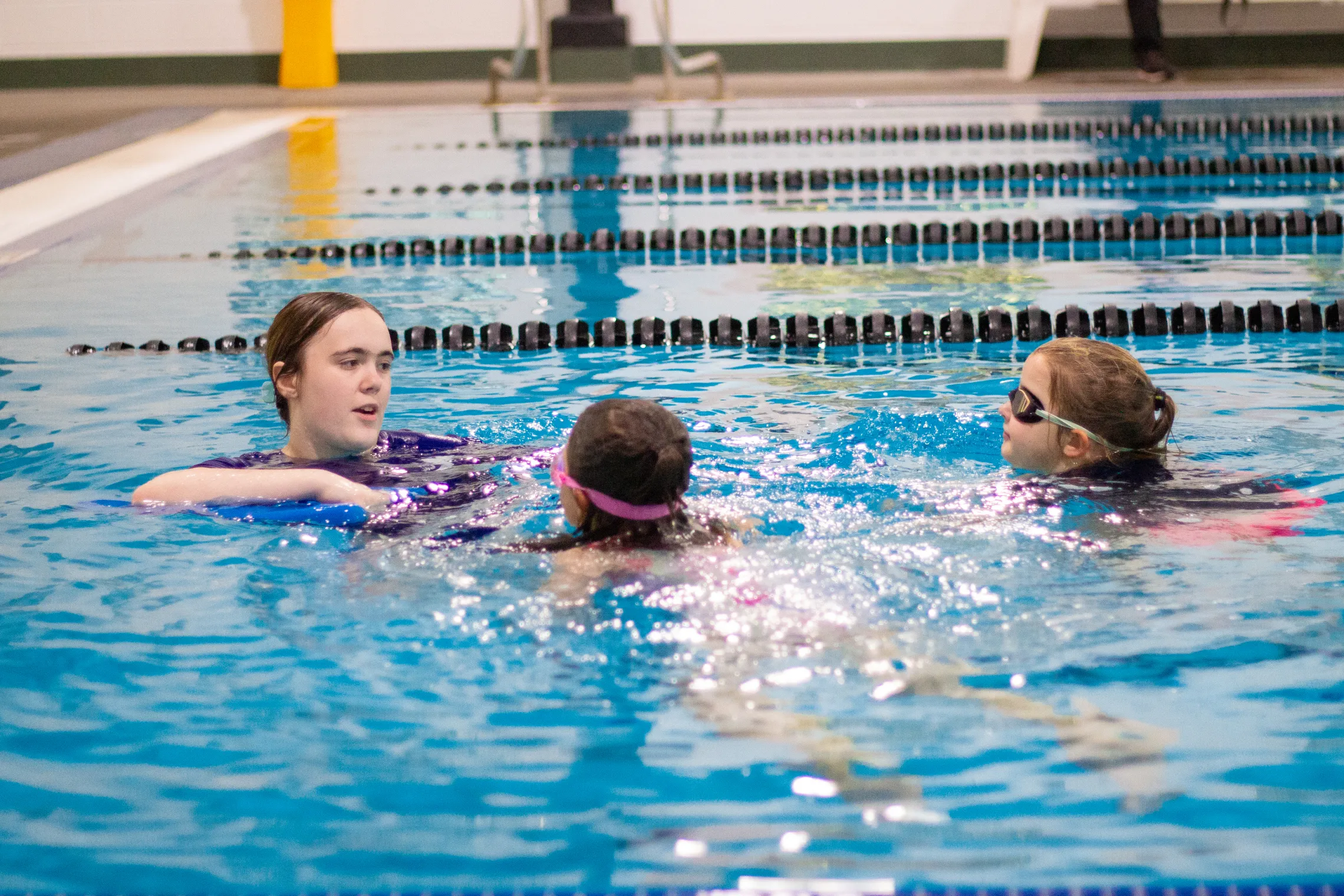 A woman teaching two kids how to swim in a pool