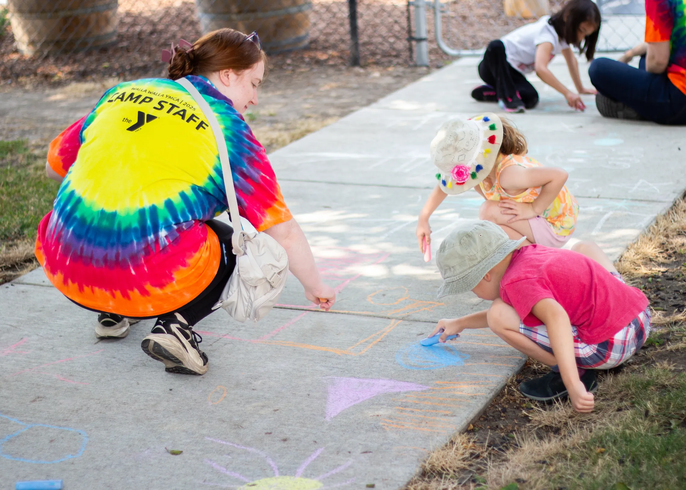 A camp staffer and kids draw chalk on sidewalk