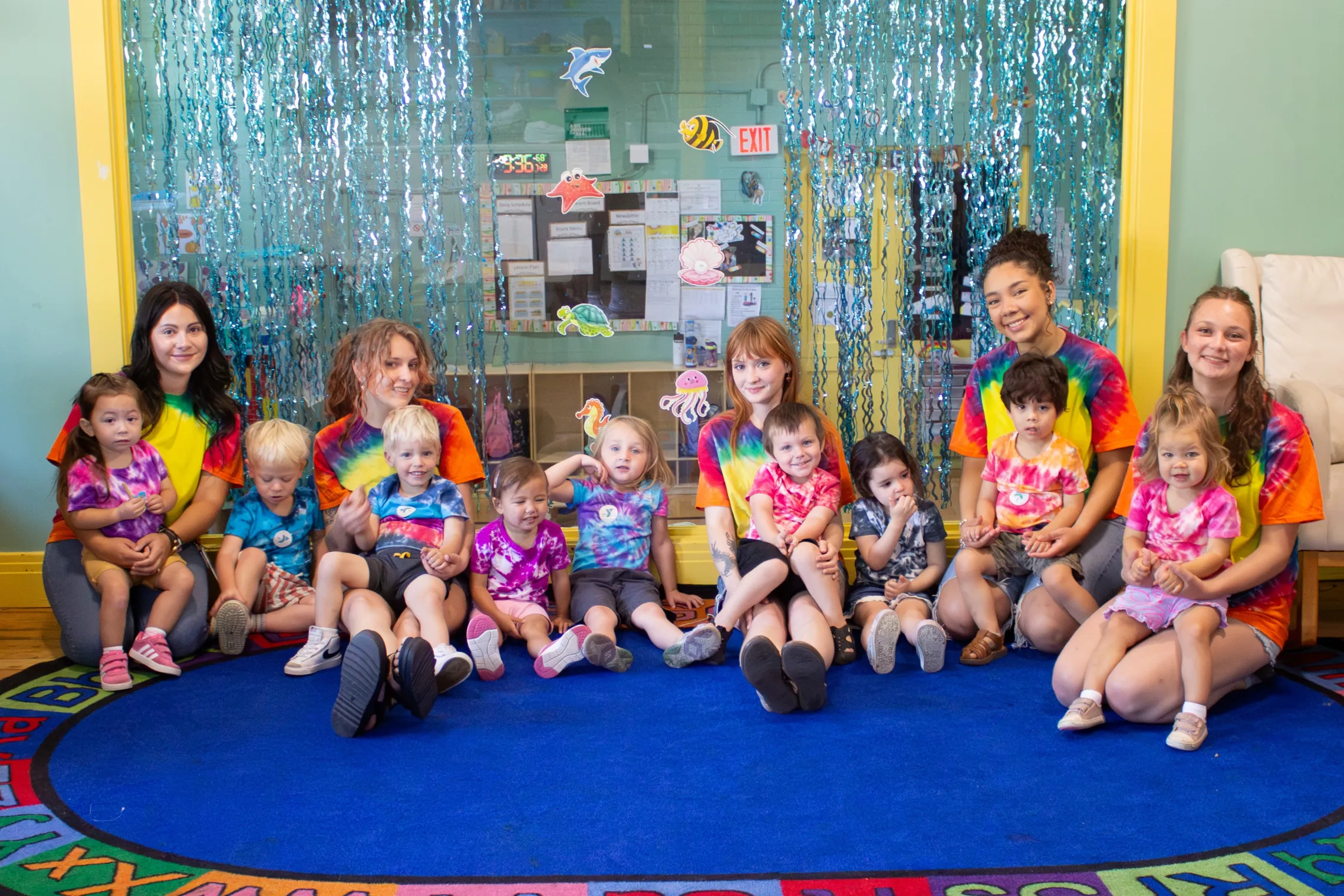 Toddlers sit in a group photo with their teachers