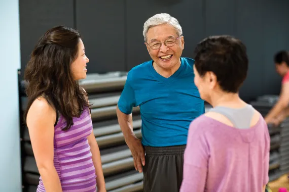 A smiling man talks to two women in a gym