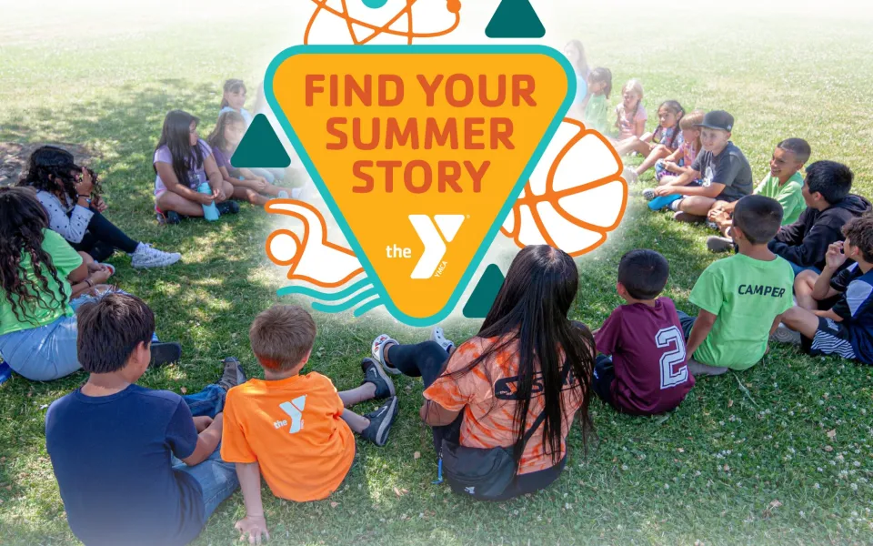 A ring of approximately 20 kids sit on a grassy field under the shade of a tree. Some shirts show the YMCA logo or lable the children as a "CAMPER". A graphic is digitally inserted into the center of the circle with the words "Find Your Summer Story" surrounded by icons of an atom, basketball, and swimmer represetning the diversity of potential stories to be found by campers.