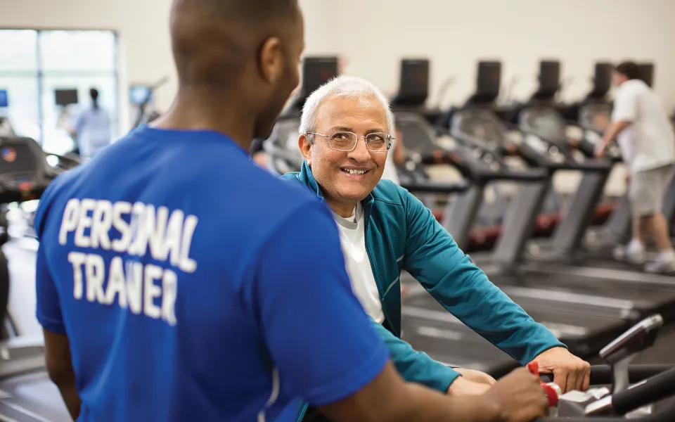 A trainer and a man having a conversation on an elliptical machine