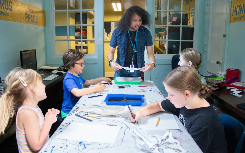 A table with art supplies, surrounded by kids and one adult