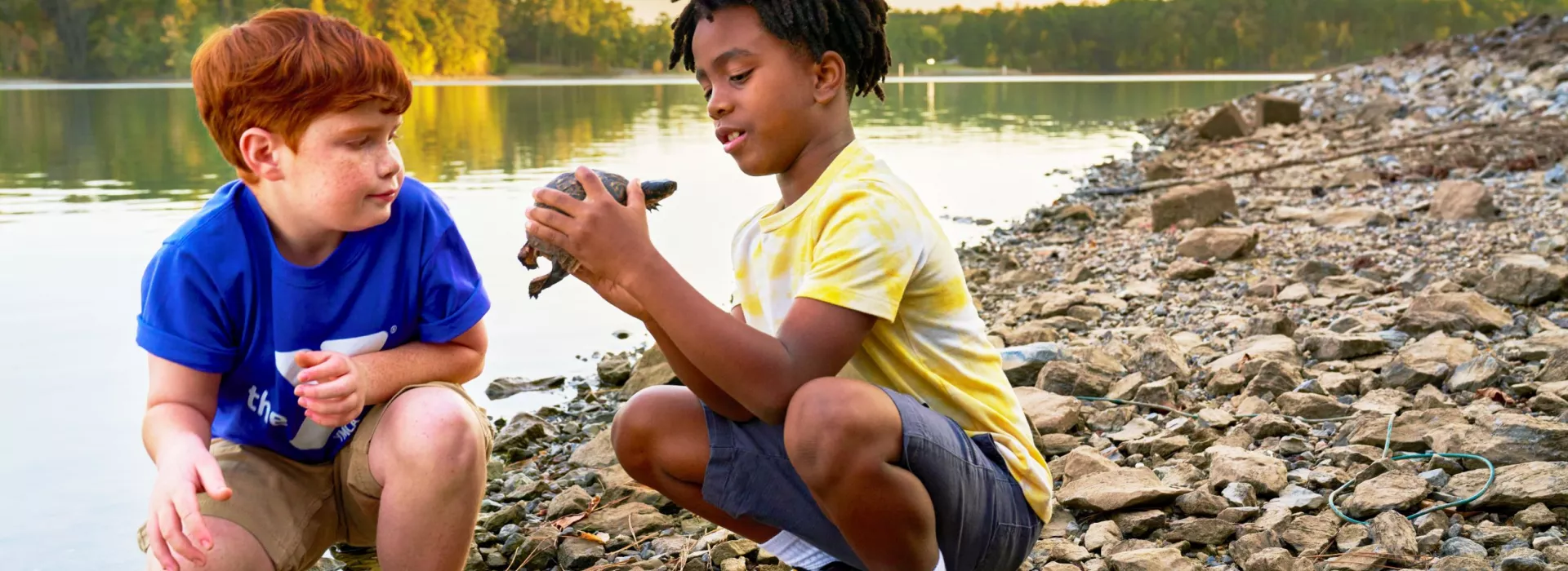 Two boys near river with turtle.