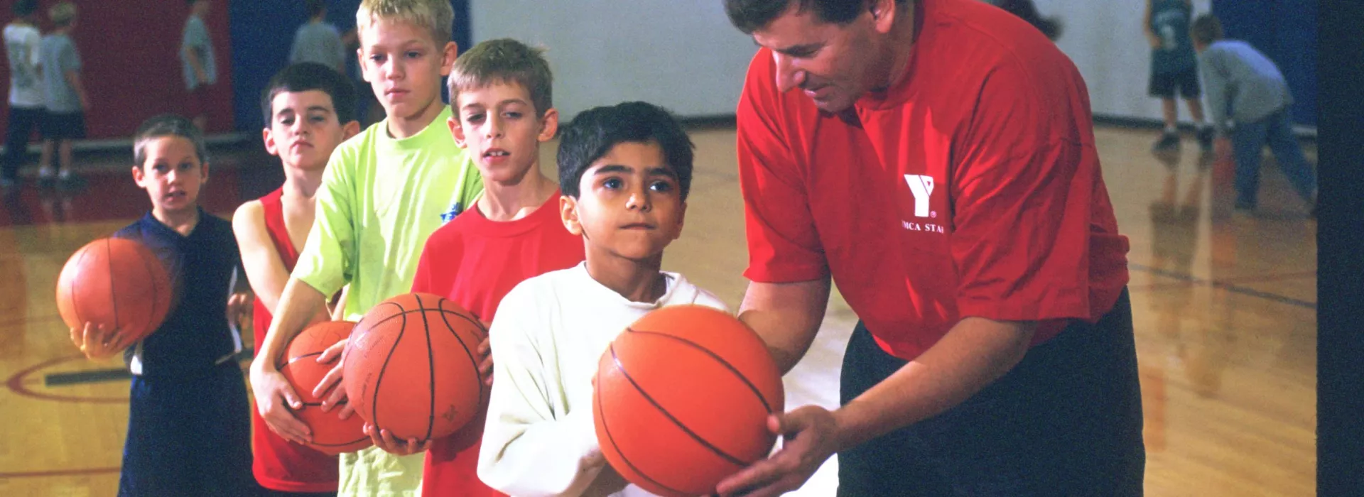 Five boys learning basketball from instructor.
