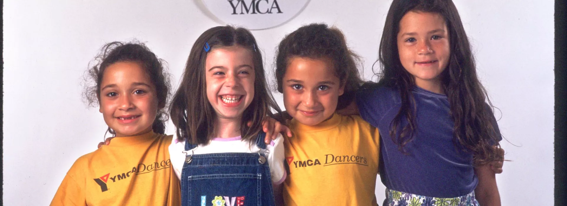 Four girls posed under an old YMCA logo.
