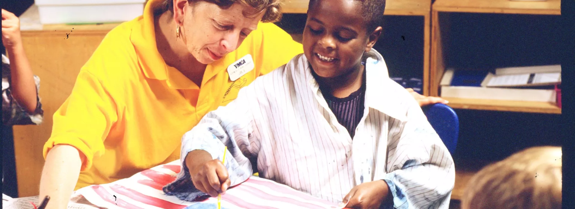 Woman observing boy painting American flag art.